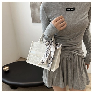 Detailed embroidery of floral patterns on off-white tote bag with silk scarf handle