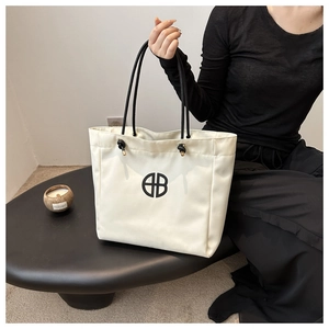 Detail of minimalist cream canvas tote bag with black rope handles and circular logo