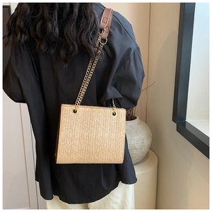 Detail of hand-woven straw shoulder bag with elegant gold chain and brown leather strap