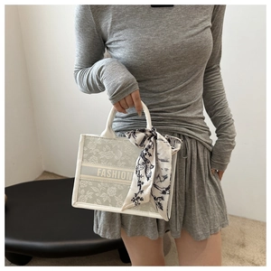 Detailed close-up of beige canvas tote bag with floral texture and silk scarf handle