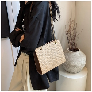 Detail of a chic straw shoulder bag featuring herringbone weave and gold chain strap
