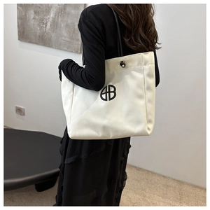 Detail view of large white canvas tote bag with black logo and shoulder strap
