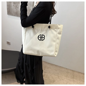 Detail of white canvas tote bag featuring black circular logo and rope shoulder strap