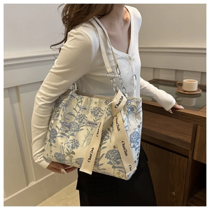 Detail of floral canvas tote bag with metal chain strap and decorative cream ribbon