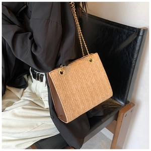 Close-up of woven straw handbag with gold chain strap and textured herringbone pattern