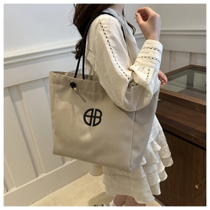 Detail of light beige canvas tote bag featuring abstract logo and black rope straps
