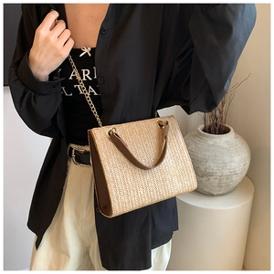 Detail of woven straw tote bag with brown leather trim and golden metal chain strap