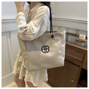 Chic beige canvas tote bag with black logo shown in a stylish lifestyle home setting