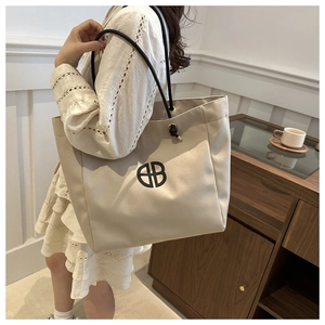 Detail of a large beige canvas tote bag with black circular EB logo and knot handle