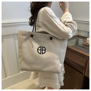 Detail of beige canvas tote bag showing black rope handles and circular geometric logo