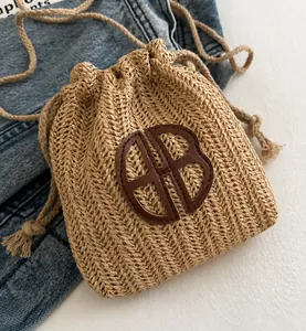 Détail du sac seau en paille tressée avec fermeture à cordon et logo en cuir marron