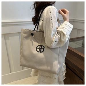 Detail of beige canvas tote bag with black rope straps and circular logo accent