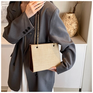 Detailed view of weave patterned tote with gold chain strap on minimalist background