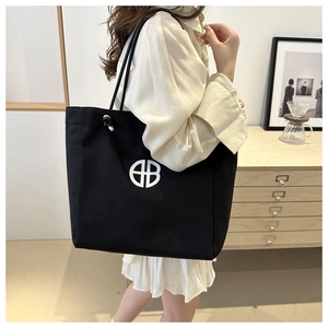 Detail of a large black canvas tote bag with a white geometric logo and slim shoulder straps