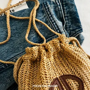 Détail d'un sac en paille tressé beige avec écusson logo en cuir marron et cordon de serrage