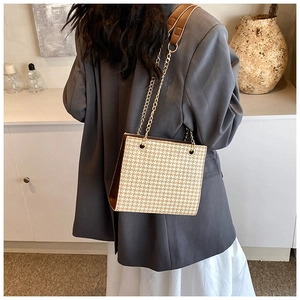 Detail of woven texture handbag with brown leather strap and gold chain on shoulder