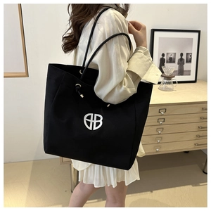 Detail of black canvas tote bag with white HB logo being carried by model in a warm room