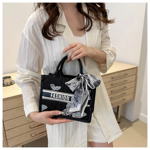 Detail of black canvas tote bag featuring white butterfly embroidery and silk scarf handle