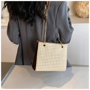 Detail of a chic woven chain shoulder bag in beige and brown worn with a gray blazer