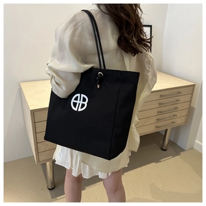 Side view of a large black canvas tote bag with white logo worn on woman's shoulder