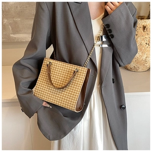 Detail of woven straw tote bag with brown leather handles and gold metal chain strap