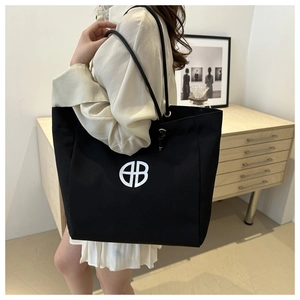 Detail of a black large-capacity tote bag with white logo and minimalist shoulder straps