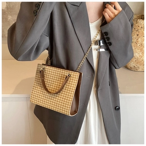 Close-up of houndstooth crossbody bag with brown leather trim and golden metal chain