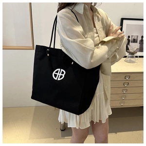 Detail of a black canvas tote bag featuring an HB logo on a model in a minimal room