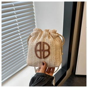 Détail du mini sac seau en paille avec logo AB en cuir et cordon de serrage en main