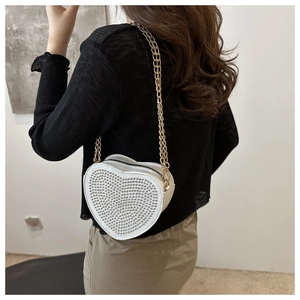Detail of heart-shaped evening bag with silver rivets and gold chain strap on model