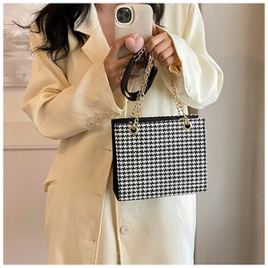 Detail of black and white houndstooth bag with gold chain strap and textured fabric