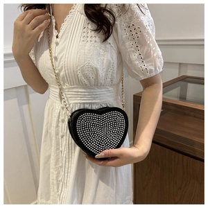 Detail shot of black heart-shaped bag with silver beads and elegant gold chain strap