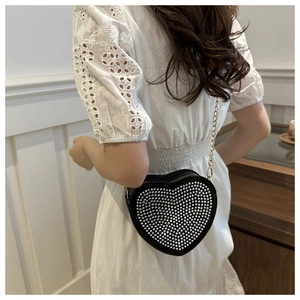 Close-up of heart-shaped black crossbody bag with silver studs on a white lace dress