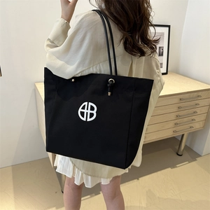 Black canvas tote bag with white circular HB logo shown on a model in a cozy interior