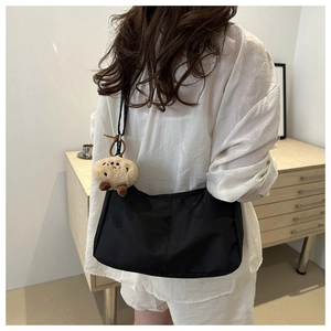 Detail of a black crescent nylon shoulder bag with a cute beige plush toy charm on the strap