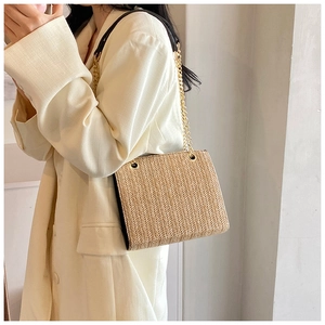 Close-up of a woven straw shoulder bag with elegant gold chain straps and black edge trim