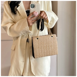 Macro detail of natural straw tote bag with black leather handle and gold metal chain