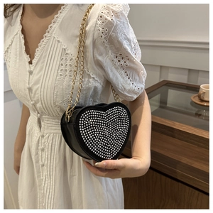 Detail of a black heart-shaped handbag with silver rhinestones and a gold chain strap