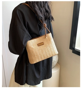 Dettaglio di una borsa a secchiello in paglia con tracolla in pelle e logo FASHION