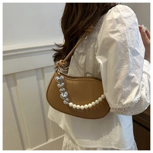 Détail du sac bandoulière en cuir marron avec chaîne perles et cœur sur robe dentelle
