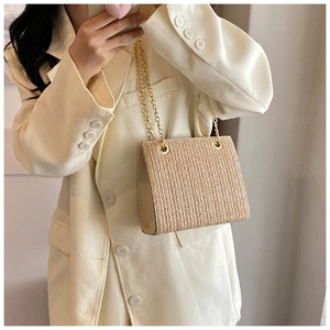 Detail of woven texture and gold chain strap on a chic crossbody bag with beige suit