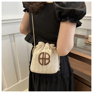 Détail du sac seau en paille avec écusson HB en cuir marron et fermeture à cordon