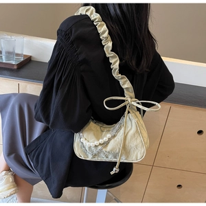 Detail of light green pleated shoulder bag with pearl chain and bow strap on model