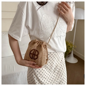 Gros plan du mini sac seau en paille tressée avec logo en cuir et bandoulière cordon