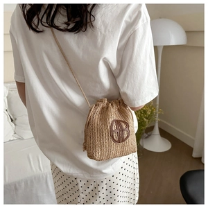 Vue arrière d'un mannequin portant le mini sac seau en paille avec logo en cuir et cordon
