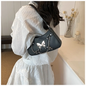 Detalle de bolso bajo el brazo negro con mariposa plateada y cadena sobre vestido blanco