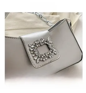 Detail shot of a silver metallic shoulder bag featuring a large square rhinestone buckle