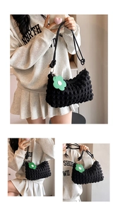 Detail of black puffy popcorn textured shoulder bag with a green flower charm