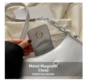 Close-up of the magnetic metal buckle and silver chain on a trendy baguette shoulder bag