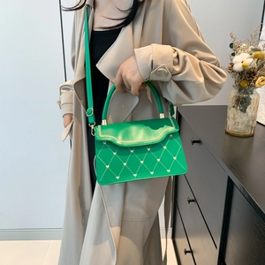 Sac à main vert avec matelassage cœur et bandoulière porté par un mannequin en trench beige